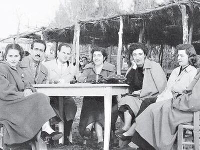 Τραπεζάκια και ψάθινες καρέκλες στην άμμο, ένα φλιτζάνι για ελληνικό / τούρκικο καφέ, μια τσάντα κι ένα ζευγάρι γυαλιά ηλίου πάνω στο τραπέζι. Ηλιόλουστη μέρα, τον χειμώνα του 1954, με την παρέα να λιάζεται στη θάλασσα, φορώντας μάλλινα παλτά