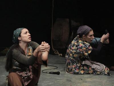 Πλάνο από την θεατρική παράσταση μέσα στο ντοκιμαντέρ “Μάνα μου Καπνοφύτισσα“, όπου αναπαριστώνται οι καπνοφύτισσες που υπέφεραν τα βράδια μετά από κάθε εξοντωτική ημέρα εργασίας με τα καπνά.